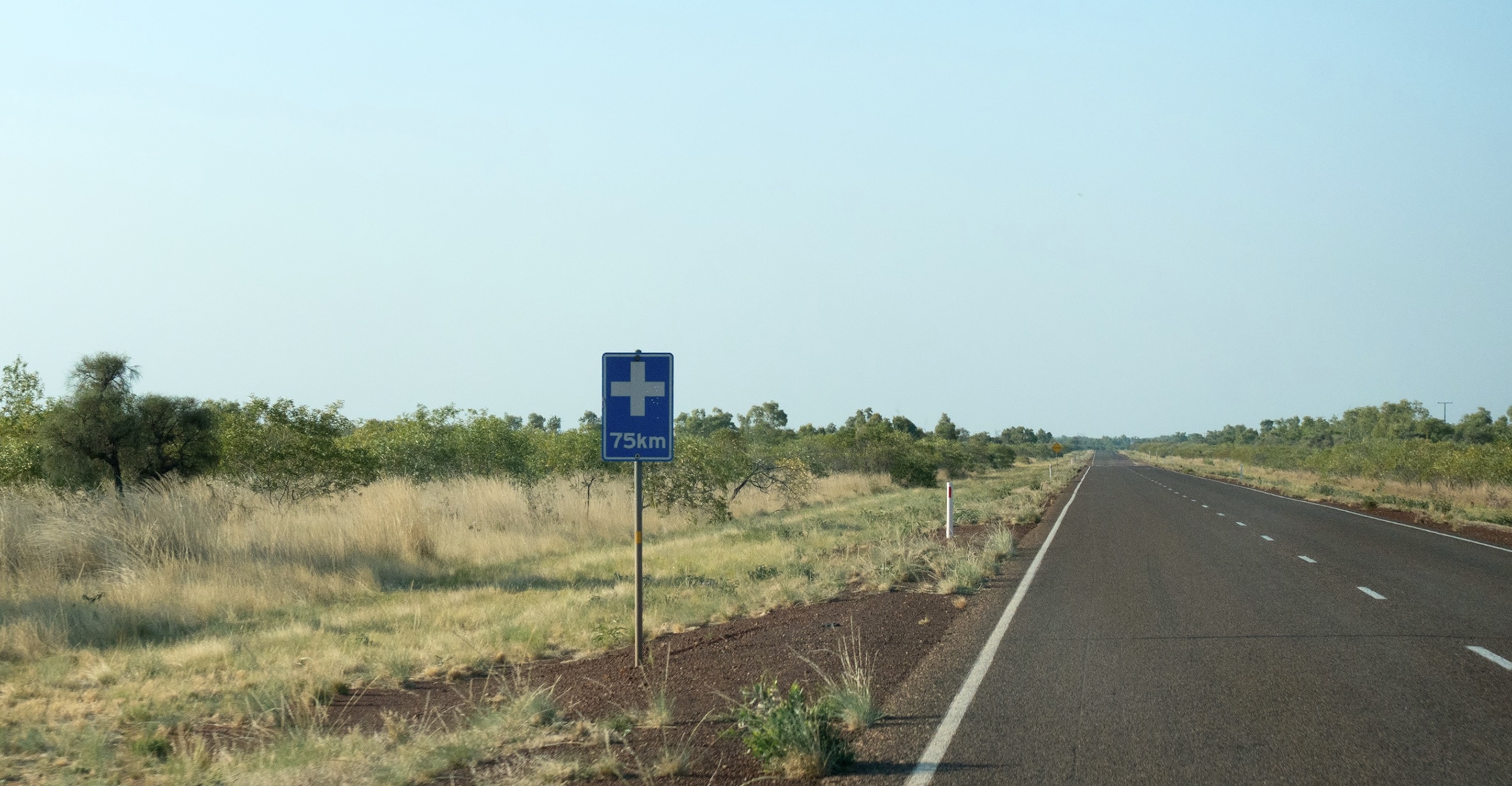 Regional road with a road sign on it. The sign reads '75km' with a hospital logo. 