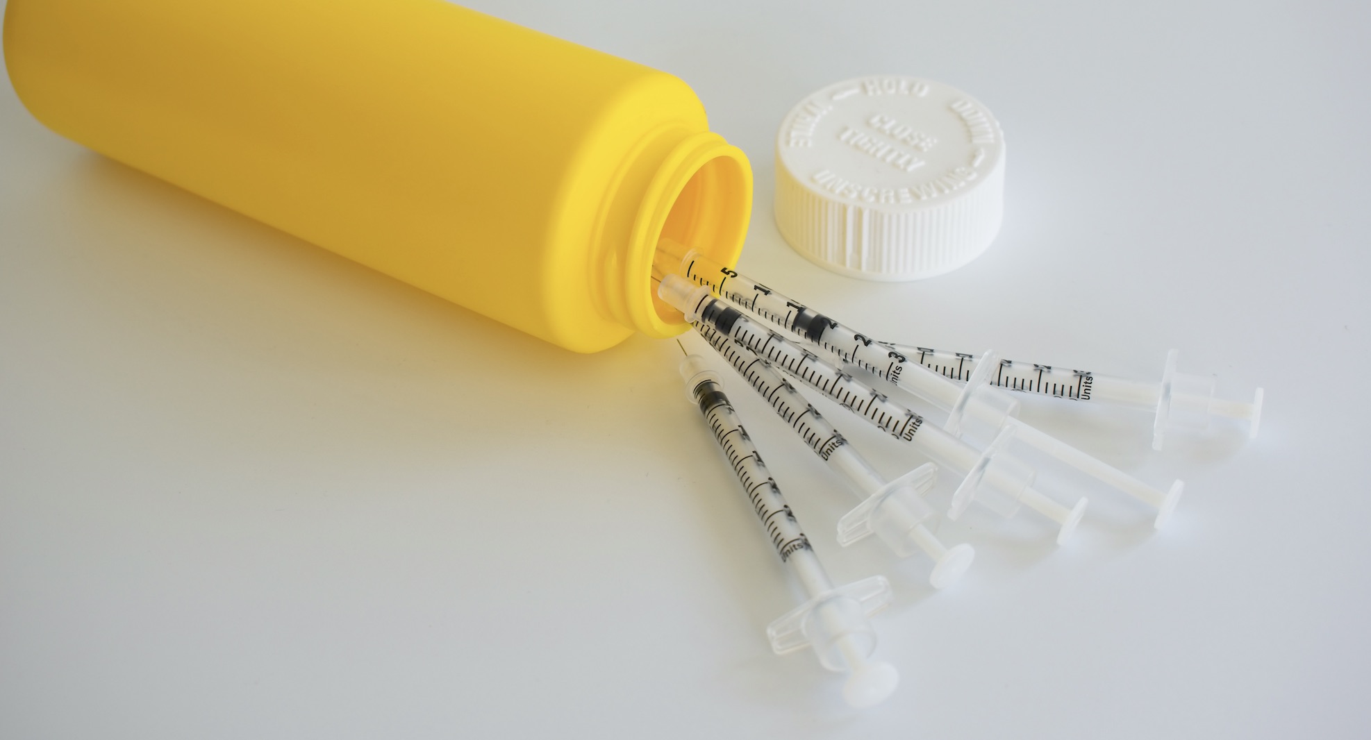 Six clean and sterile syringes and a yellow sharps disposal bin.