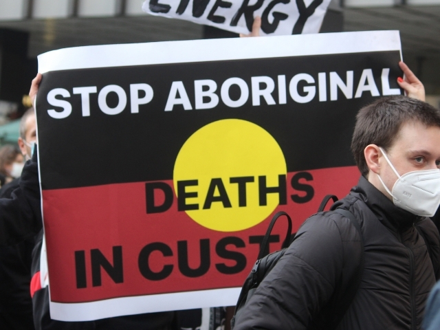 Protest sign with the Aboriginal flag with the text "stop Aboriginal deaths in custody".