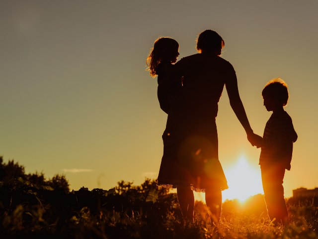 A person holding two children at sunset.