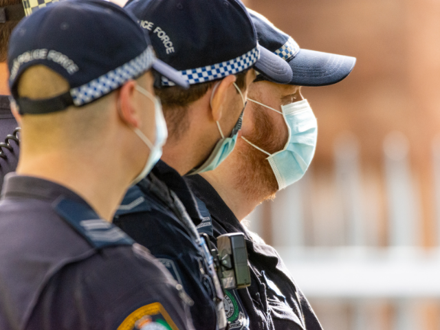 Three police standing in a line wearing surgical face masks.