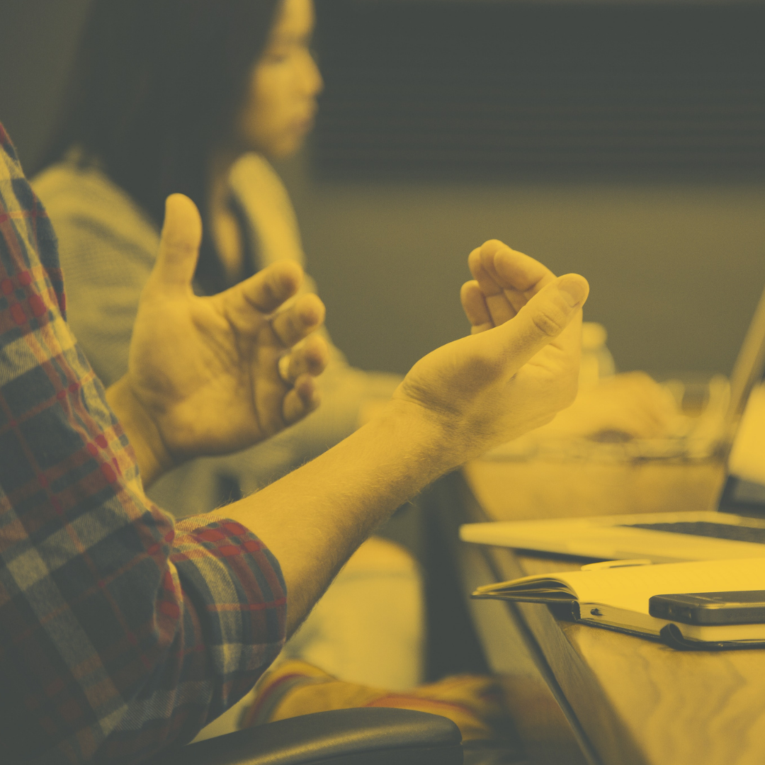 A person gesturing in a meeting, with a yellow and grey filter over the top.