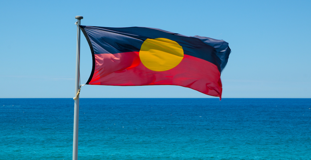 An Aboriginal flag flying in front of turquoise ocean. 