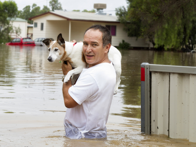 A man holding a dog on his shoulders in flood waters.