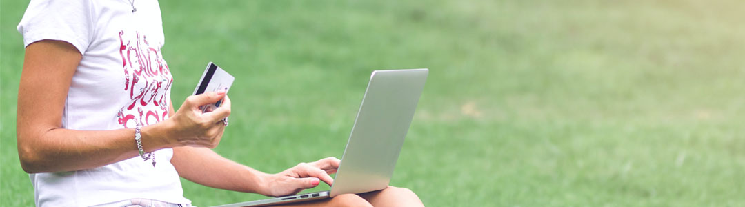 A person sitting on the grass holding a credit card.