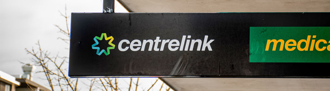 A white Centrelink logo on a dark shop front sign.