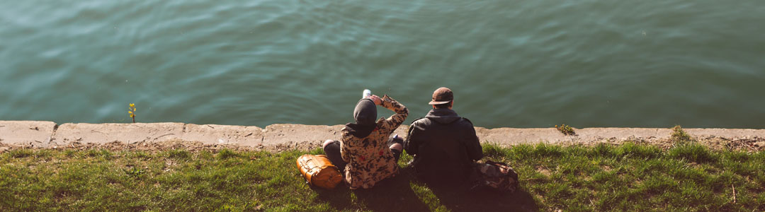 Two people in the distance sitting in front of a lake. 