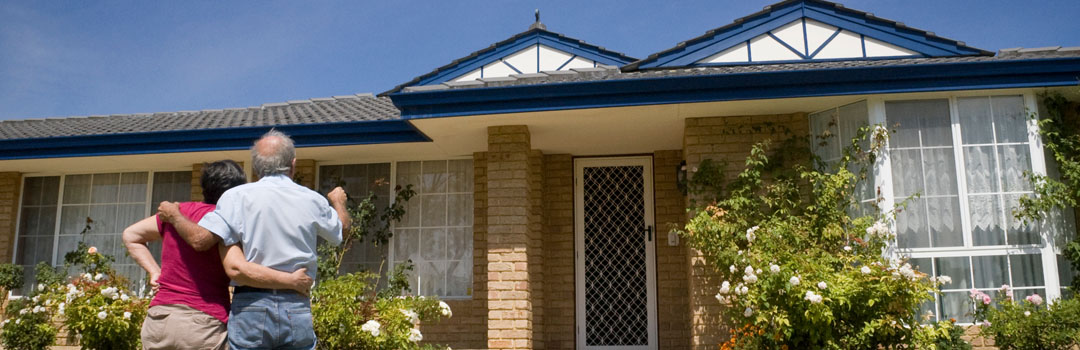 Two older people standing in front of a brick house.