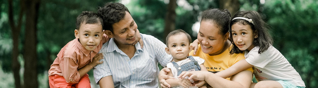 Two parents with three young children sitting outdoors. Everyone is laughing. 