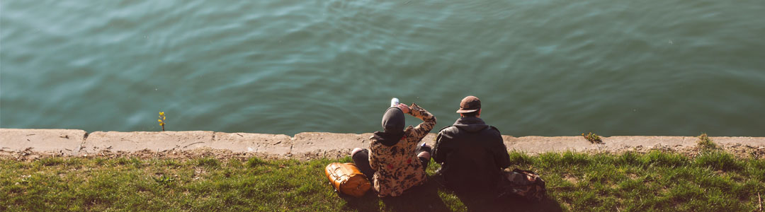 Two people sitting in the distance on the edge of a lake.