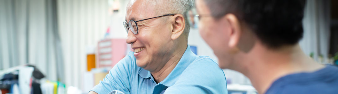 A South Asian man wearing a light blue polo shirt and glasses smiling in a hospital.