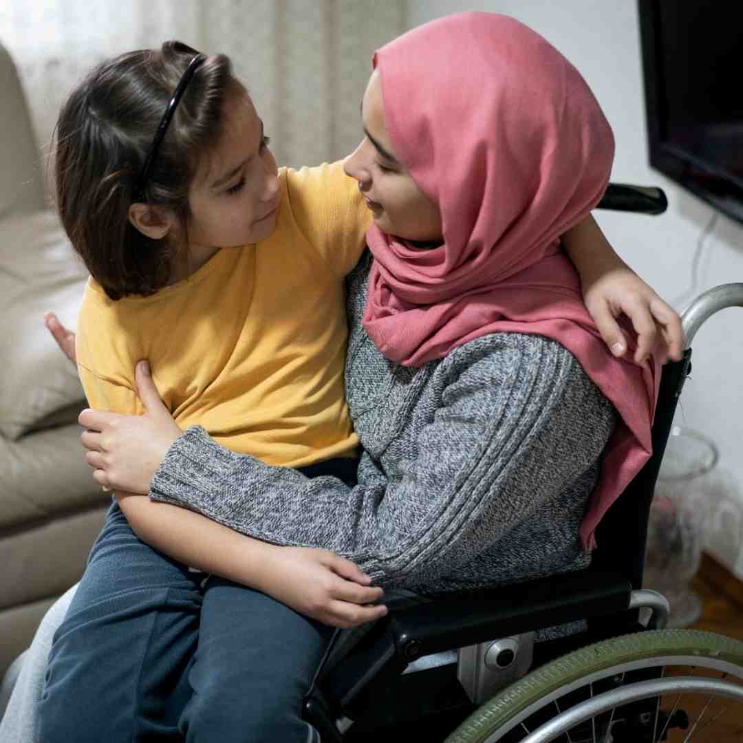 A woman who uses a wheelchair and wears a pink headscarf with a young child.