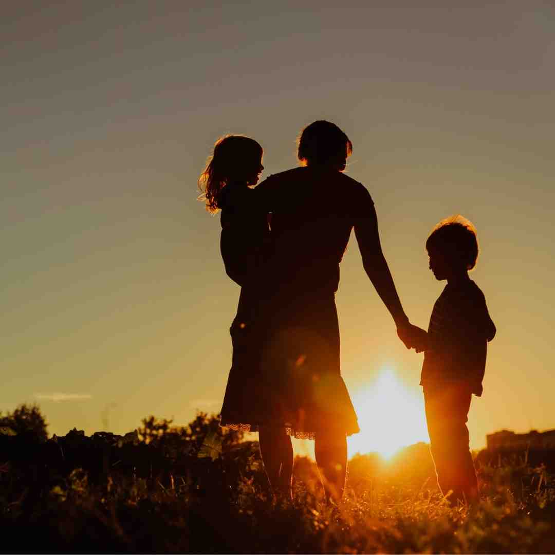 Silhouette of a parent with two kids at sunset.