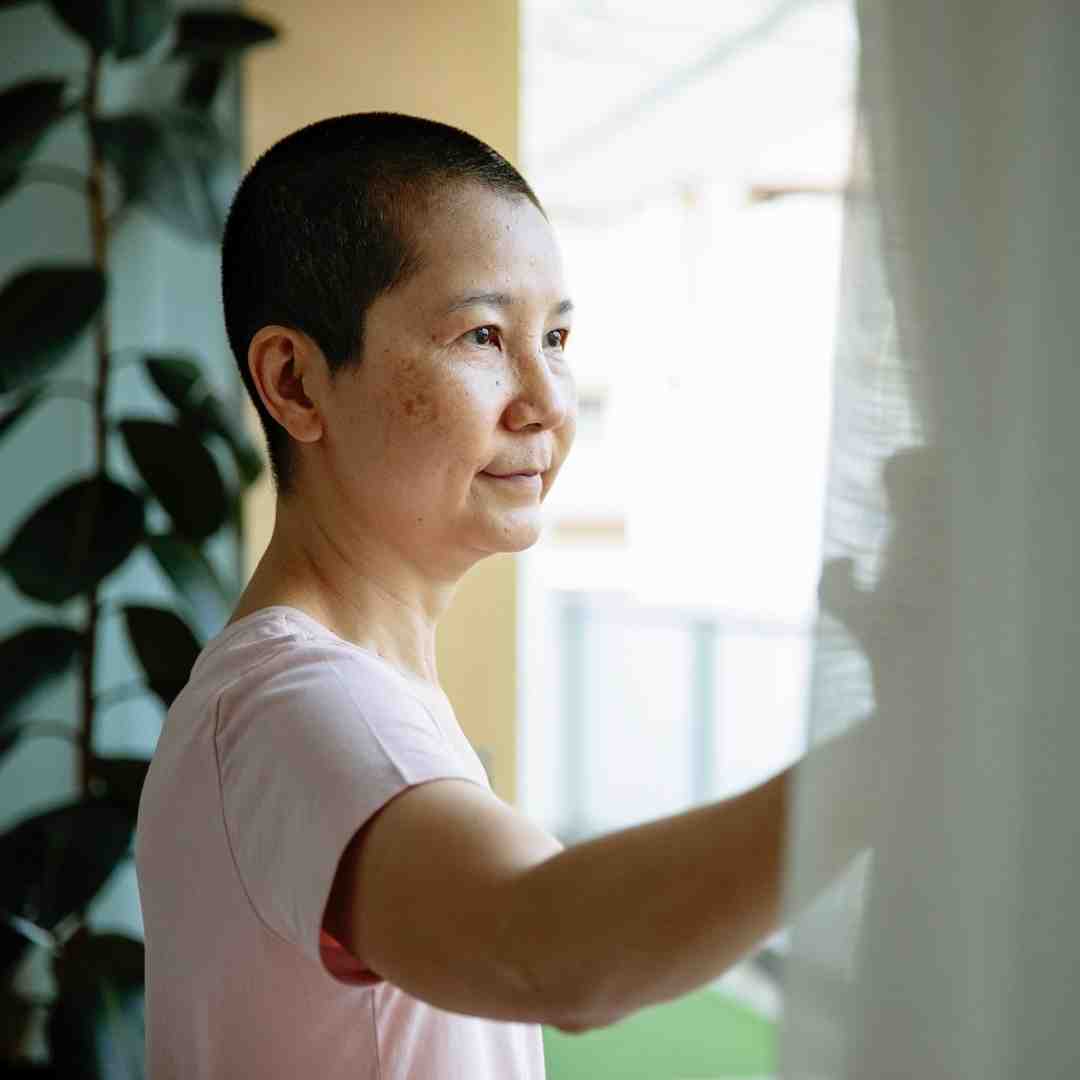 A woman with a shaved head standing in front of a window. 
