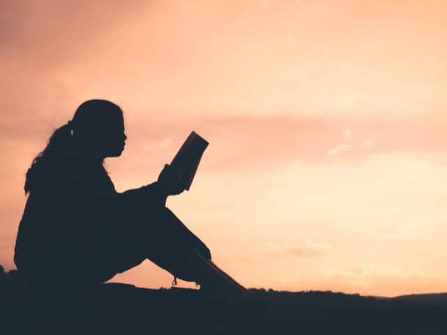 Silhouette of a woman at sunset reading a book. 