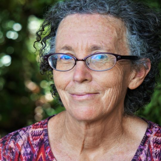 Portrait of a woman with light coloured skin and small dark glasses smiling. 