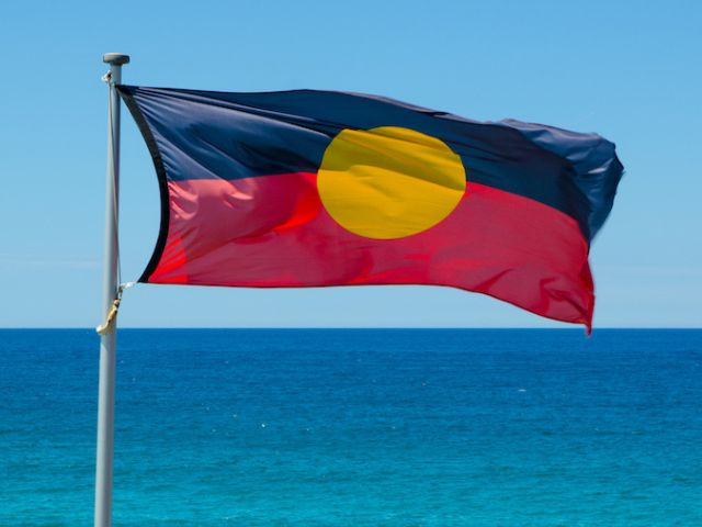 An Aboriginal flag flies in front of the ocean.
