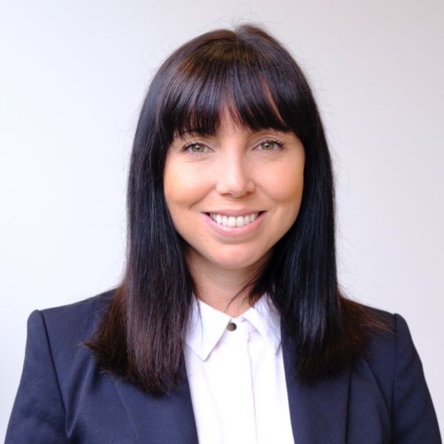 A woman with a dark fringe, wearing a white shirt and blazer, smiling. The photo is a headshot.