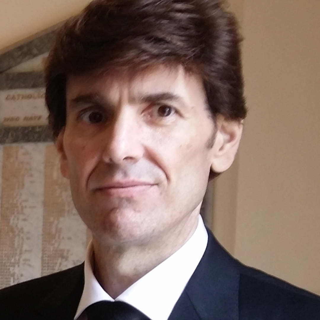 Close-up of a man with brown hair looking at the camera. He is wearing a tie.