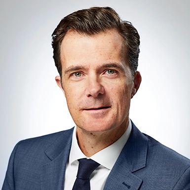 A white man in a suit and tie smiling slightly.