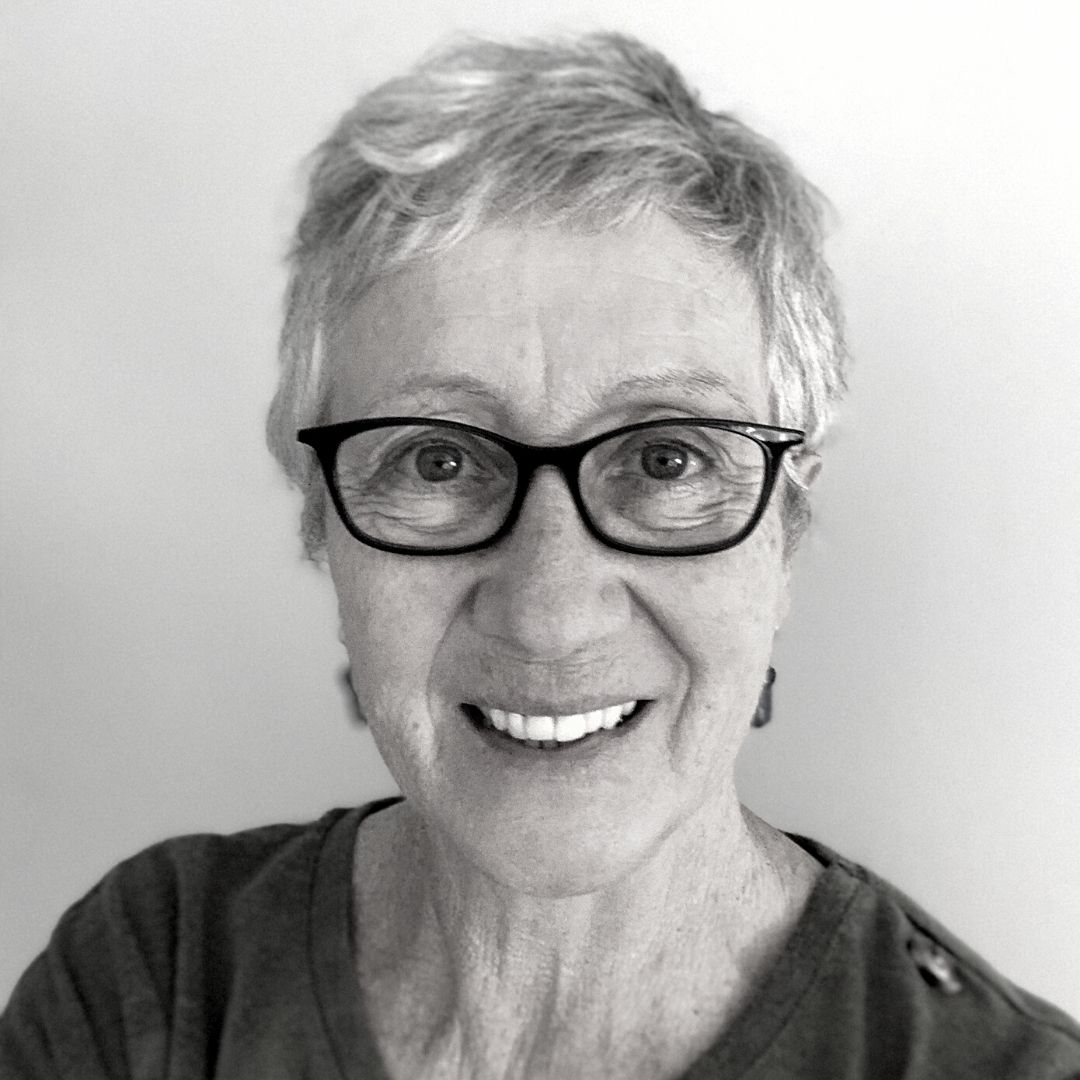 Photo of Julie Robson smiling from the chest up. She wears dark glasses and earrings, and has short grey hair.