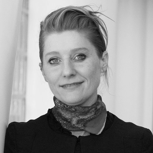 Photo of a person with long hair tied up, wearing a scarf and smiling slightly.