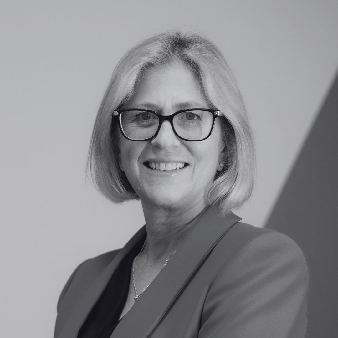 Headshot of Melanie Noden smiling. She has blonde, shoulder-length hair and wears dark glasses and a blazer.