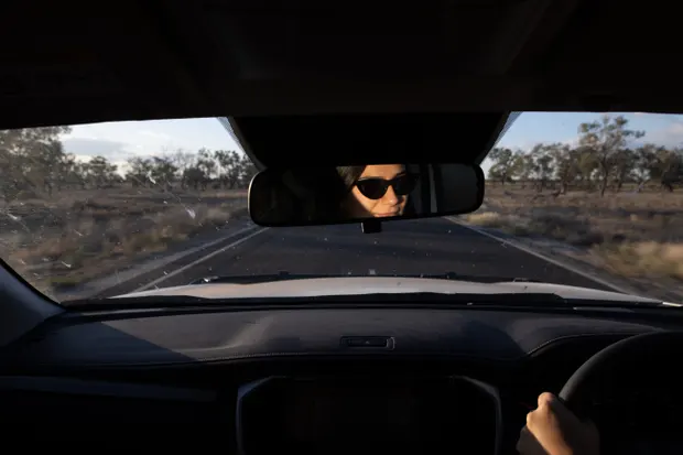 A woman driving on a rural road at sunset.