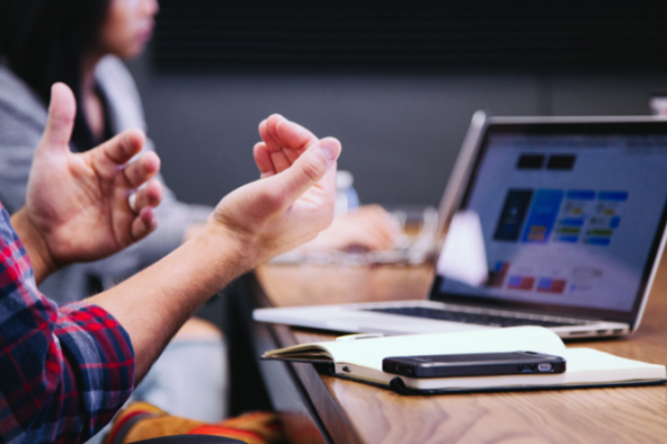 A person at a desk with laptop holds hands up. 