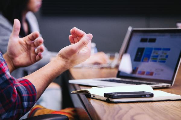 A person at a desk with laptop holds their hands up. 