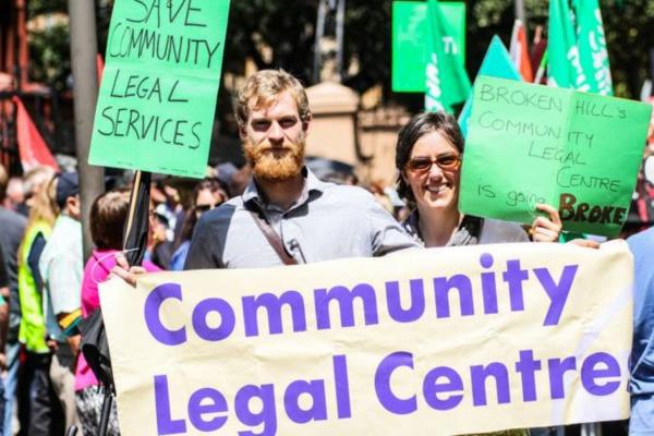 Person holding community legal centre banner in a crowd. 