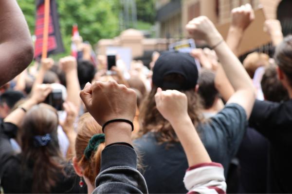 A person holds a fist up at a protest outside NSW Parliament House.